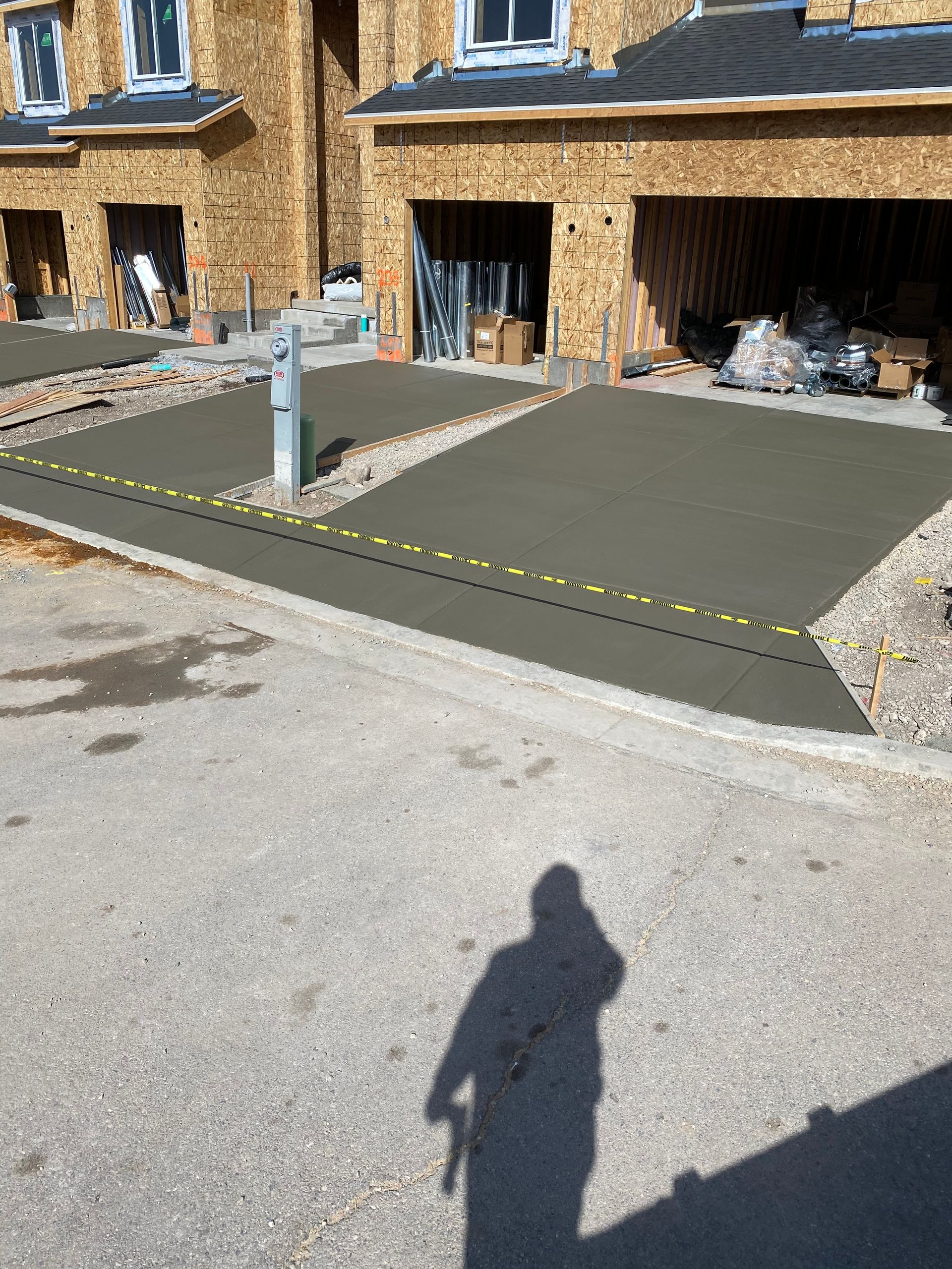 Concrete driveway under construction in front of townhouses, with a person's shadow in the foreground.