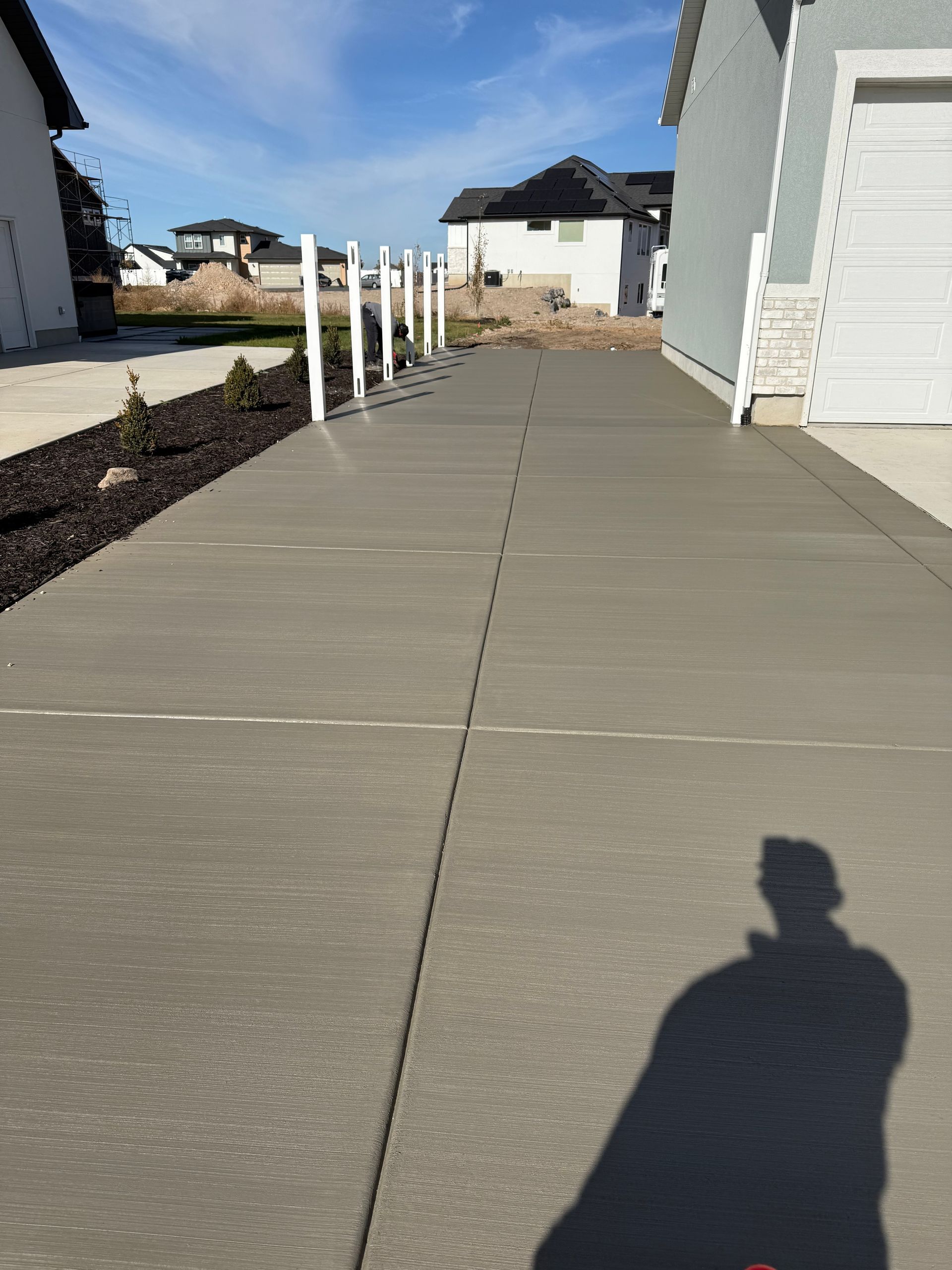 Concrete driveway leading to a garage with white posts on the side, sunny day.